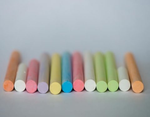 Quadrado - Gizes de cera coloridos uns ao lado do outro em fundo cinza o instrumento é muito utilizado pelo professor
